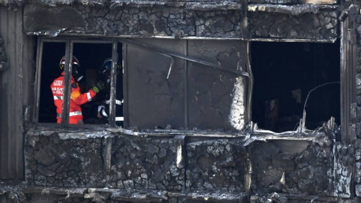 Des pompiers inspectent ce qu'il reste de la tour Grenfell ravagée par un incendie, le 16 juin 2017 à Londres.
