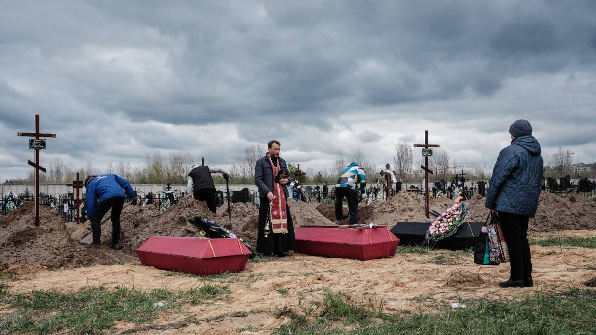 Nadia (à droite) assiste aux funérailles de son mari et de deux autres victimes tuées, menées par Andrii Holovine (au centre), prêtre de l'église Saint-André Pervozvannoho, dans un cimetière de Boutcha, le 18 avril 2022.

