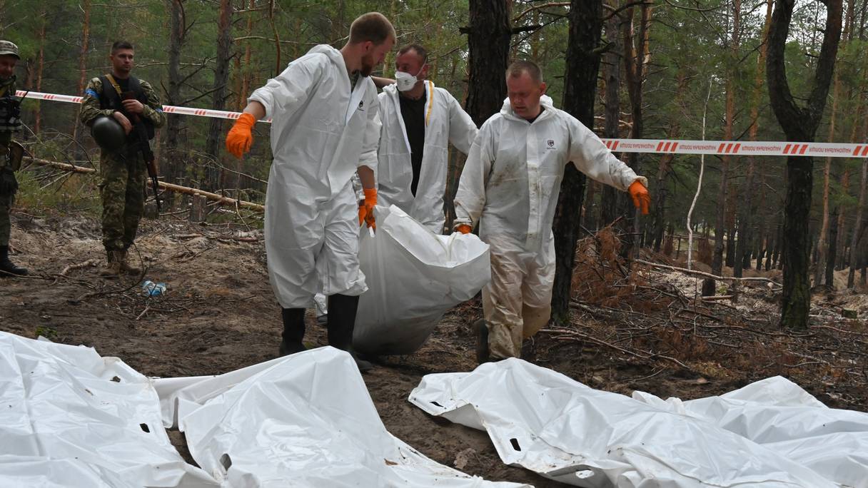 Des membres de la police scientifique ukrainienne portent une dépouille dans la forêt d'Izioum, dans l'est de l'Ukraine, le 16 septembre 2022.
