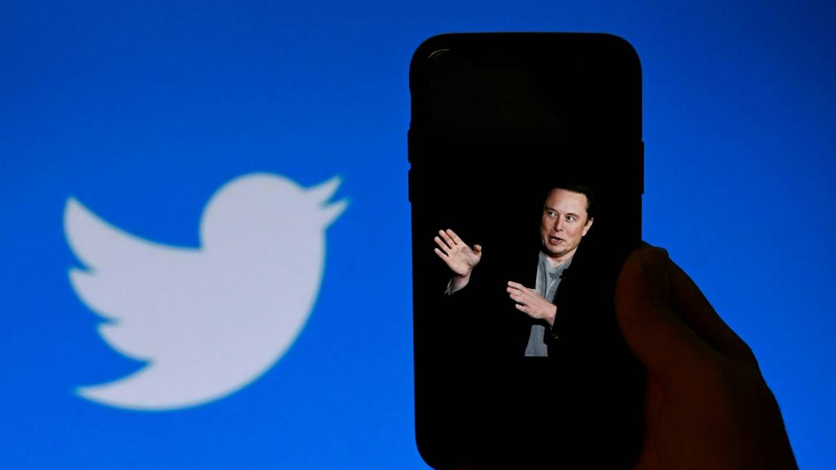 Elon Musk sur un smartphone, et le logo de Twitter à l’arrière-plan, le 4 octobre 2022. Le propriétaire de Twitter a acté le 24 novembre 2022 l’amnistie générale des comptes suspendus, après un sondage informel auquel ont participé 3,16 millions d’utilisateurs. 
