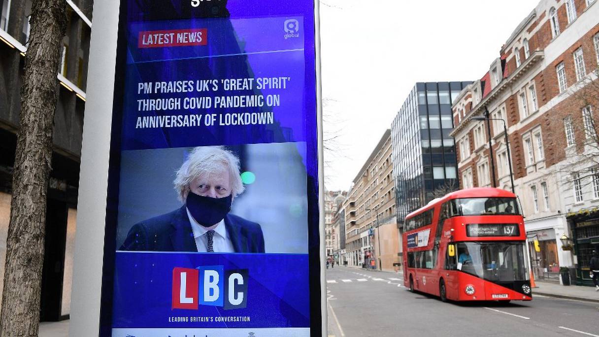 Un panneau publicitaire électronique affiche un reportage de la chaîne TV LBC, dans lequel le Premier ministre britannique Boris Johnson a fait l'éloge du "grand esprit" avec lequel les gens ont fait face au troisième confinement en Angleterre, à Londres, le 23 mars 2021. 
