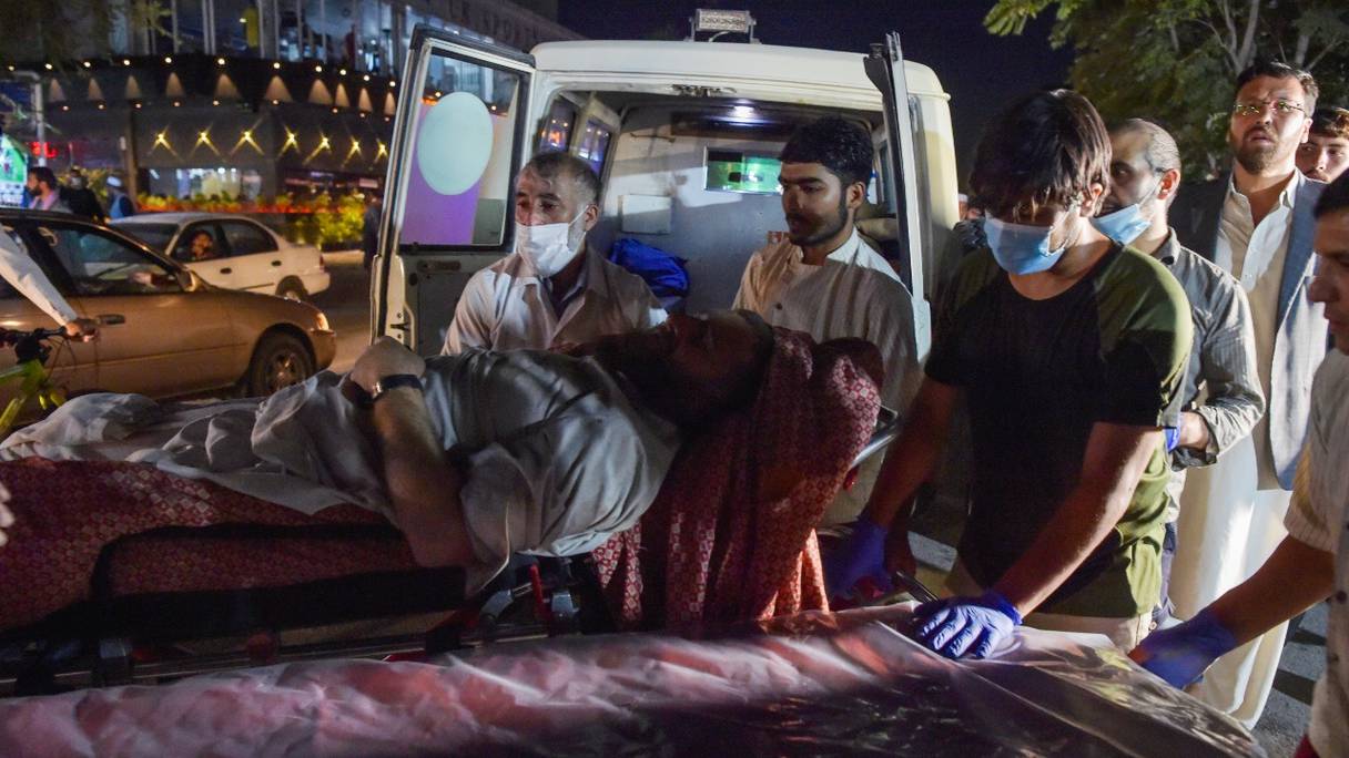Des volontaires et du personnel médical amènent un homme blessé pour qu'il soit soigné après deux puissantes explosions, qui ont fait au moins six morts, devant l'aéroport de Kaboul le 26 août 2021.
