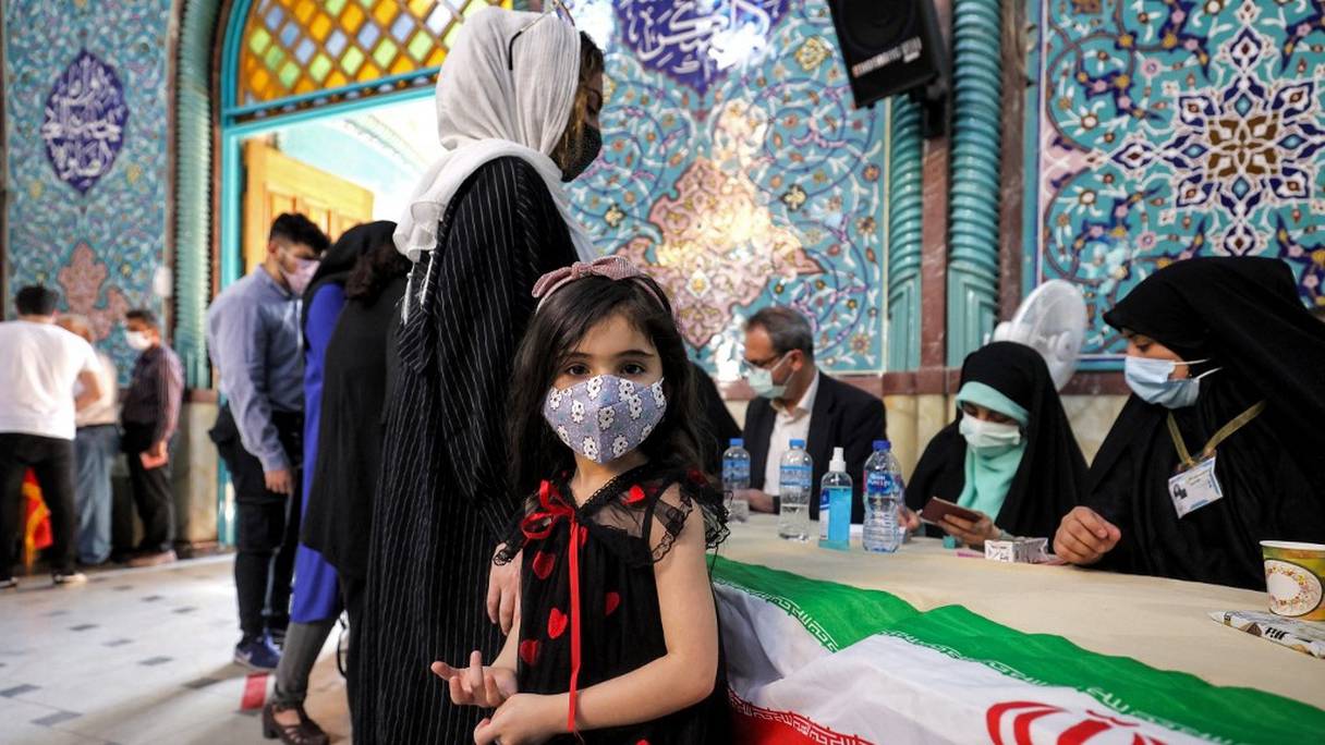 Une petite fille regarde l'objectif, alors qu'une femme s'inscrit pour aller voter dans un bureau de vote de la capitale iranienne, Téhéran, le 18 juin 2021, lors de l'élection présidentielle de 2021. 
