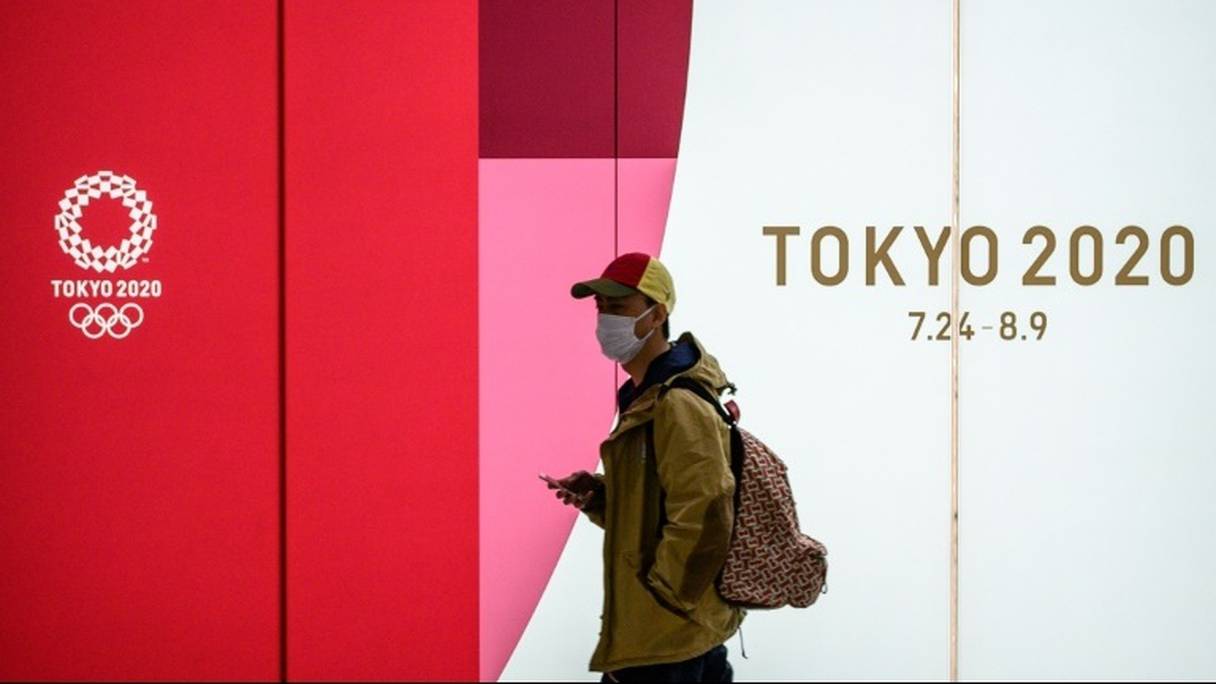 Un homme portant un masque dans le métro passe devant une affiche des Jeux olympiques Tokyo 2020 le 11 mars 2020 à Tokyo.
