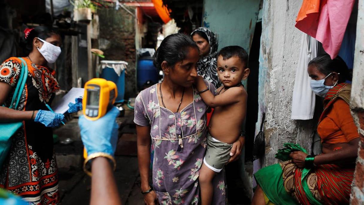 Un employé de la santé publique indienne prend la température corporelle d'une femme et de son enfant dans une ruelle de Bombay.
