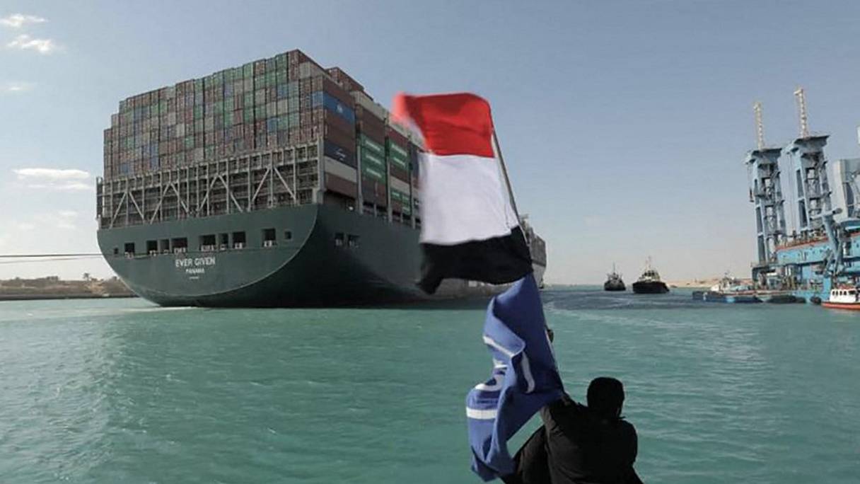 Un homme agite un drapeau égyptien, le 29 mars 2021, après que le porte-conteneurs Ever Given ait été complètement délogé des rives du canal de Suez. Le canal de Suez a rouvert, après une semaine de blocage d'une artère majeure pour le commerce mondial. 
