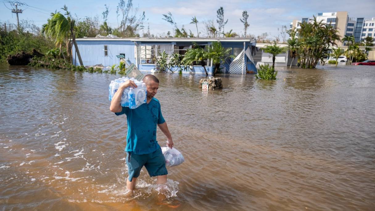 Un homme qui transporte des bouteilles d'eau patauge dans un quartier inondé, suite au passage de l'ouragan Ian, à Fort Myers, en Floride, le 29 septembre 2022.
