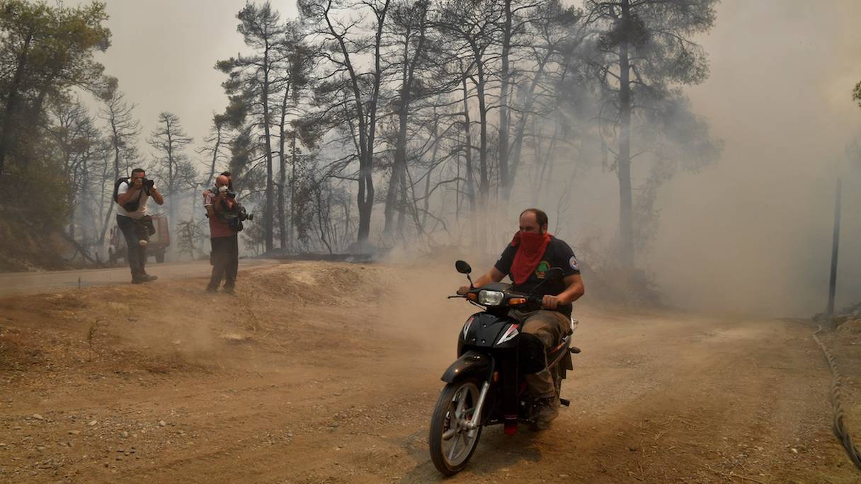 Un homme conduit un scooter sur une route ravagée par un incendie près d'un village grec tandis que les pompiers se battaient pour maîtriser deux incendies majeurs alors que le pays étouffe sous une vague de chaleur record. 
