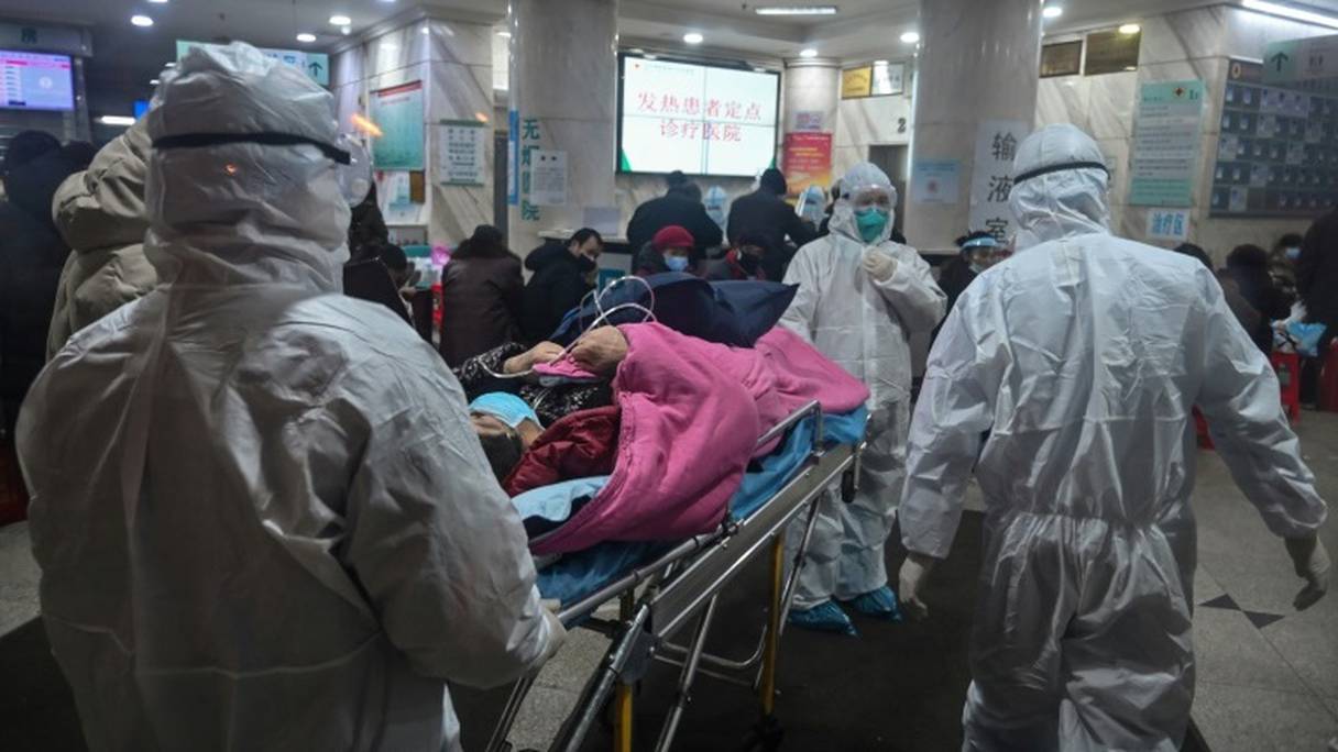 Du personnel médical en combinaison de protection arrivent à l'hôpital de la Croix-Rouge de Wuhan avec un patient, le 26 janvier 2020.
