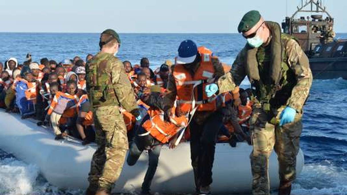 Des soldats de la marine anglaise aident des migrants à descendre d'un canot de sauvetage après avoir été sauvés d'un naufrage au large des cotes de Libye. 
