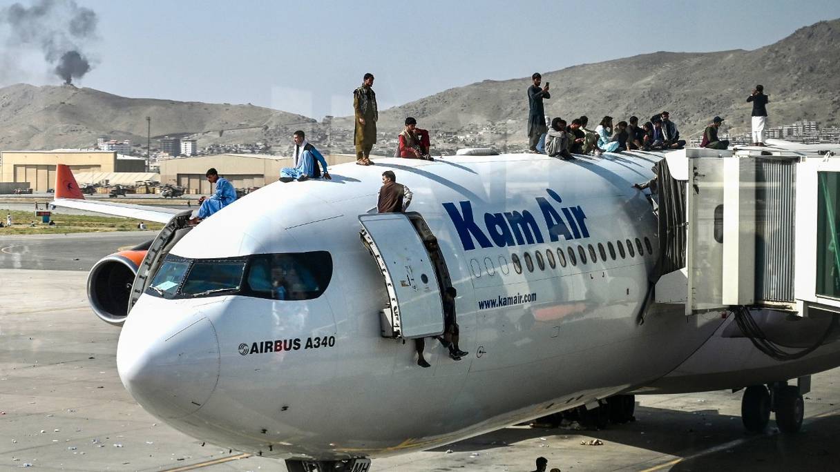 Des Afghans au sommet d'un avion à l'aéroport de Kaboul, le 16 août 2021, après une fin étonnamment rapide à une guerre de 20 ans en Afghanistan. Des milliers de personnes sont rassemblées à l'aéroport de la capitale et tentent de fuir les Talibans.
